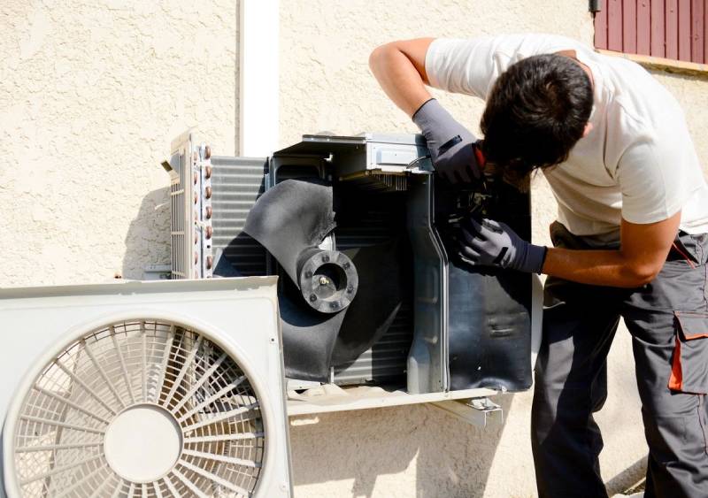 Young man electrician installer working on outdoor compressor unit air conditioner