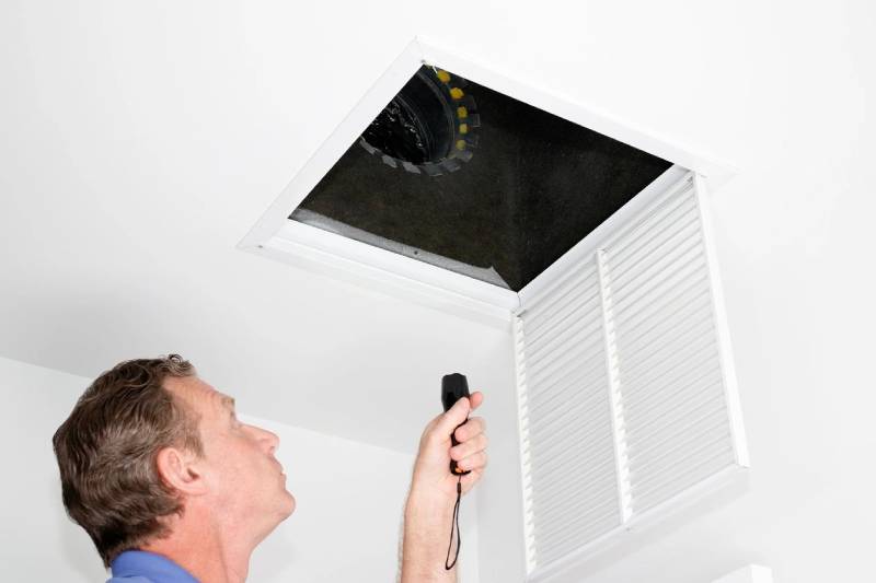 A man is looking at the air vent in his home.