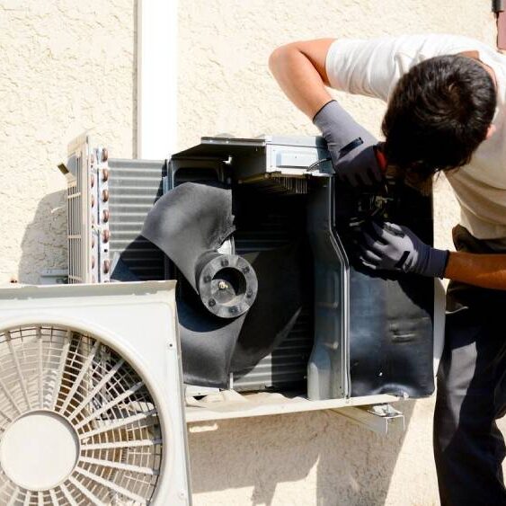 Young man electrician installer working on outdoor compressor unit air conditioner